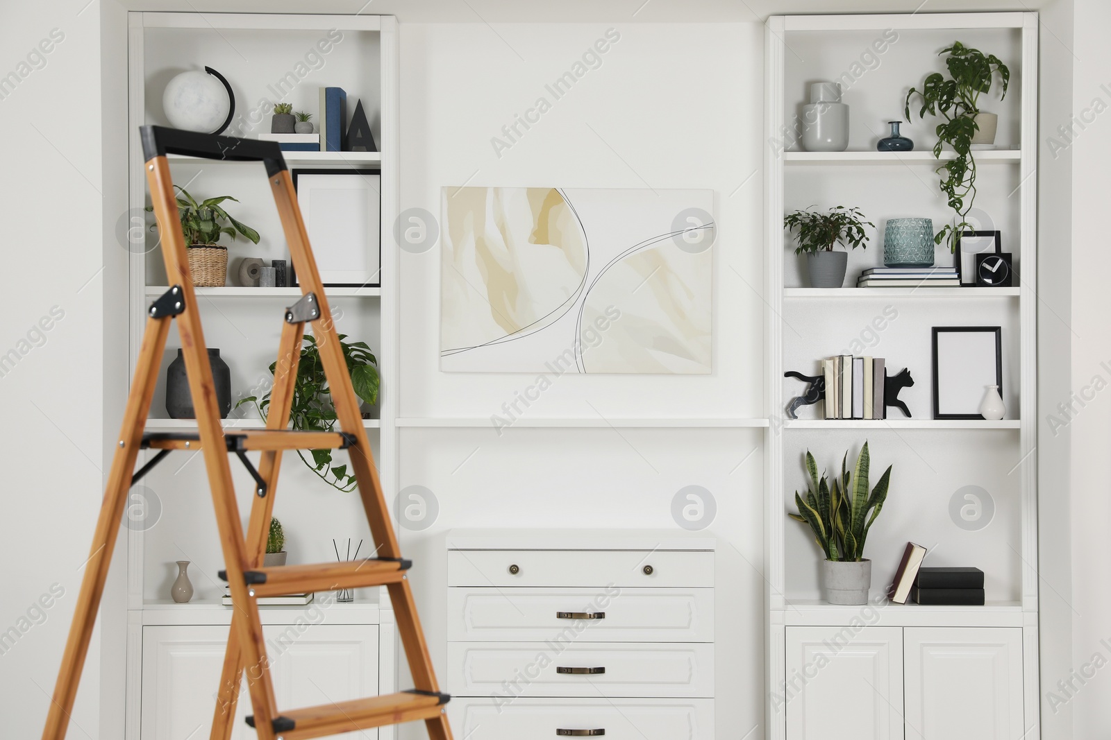 Photo of Wooden folding ladder near chest of drawers and shelves with accessories indoors