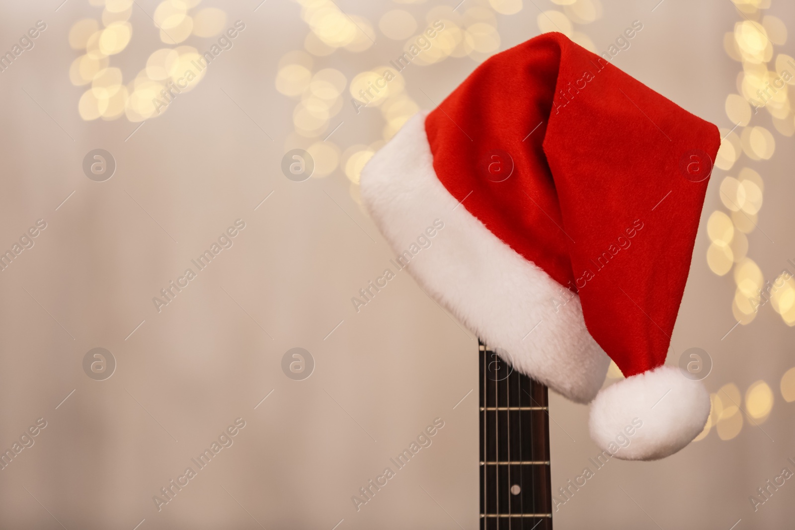 Photo of Guitar with Santa hat against blurred lights, space for text. Christmas music