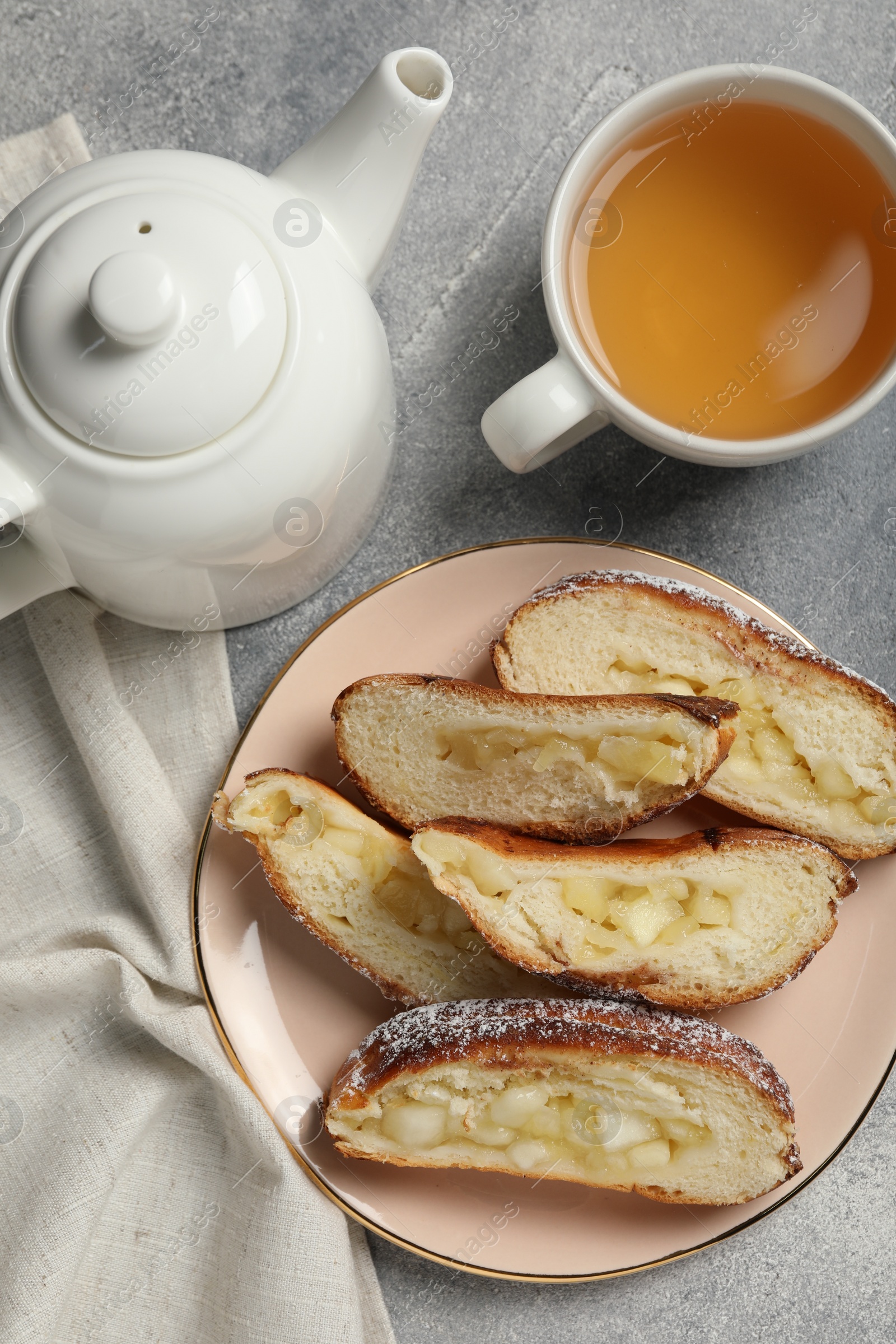 Photo of Pieces of delicious yeast dough cake and tea on light gray table, flat lay