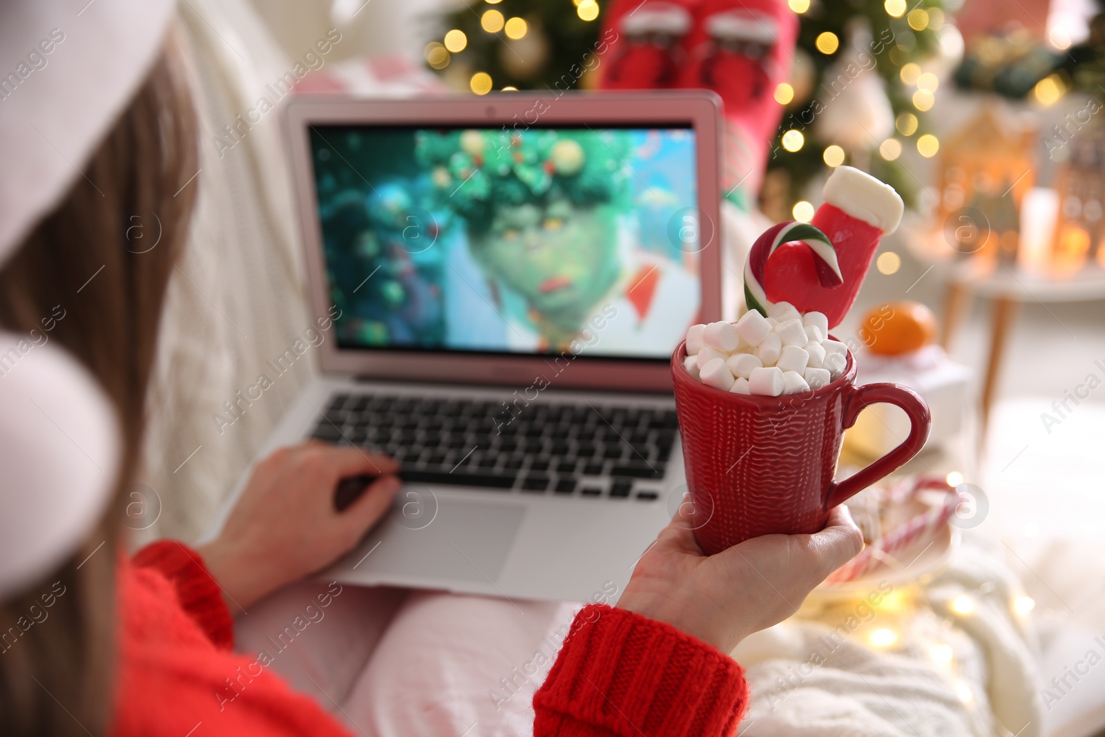 Photo of MYKOLAIV, UKRAINE - DECEMBER 25, 2020: Woman with sweet drink watching The Grinch movie on laptop at home, closeup. Cozy winter holidays atmosphere