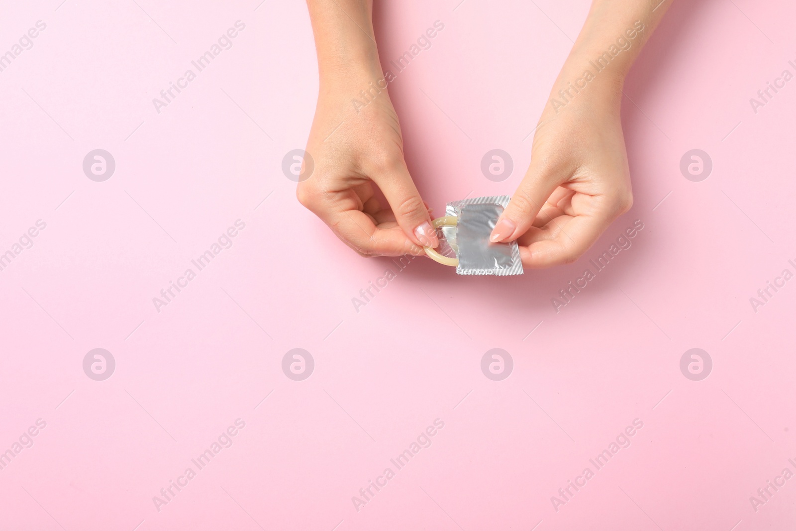 Photo of Young woman with condom on pink background, top view with space for text. Safe sex