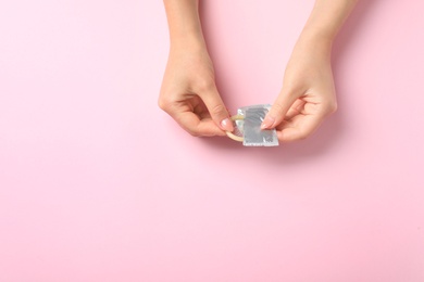 Young woman with condom on pink background, top view with space for text. Safe sex