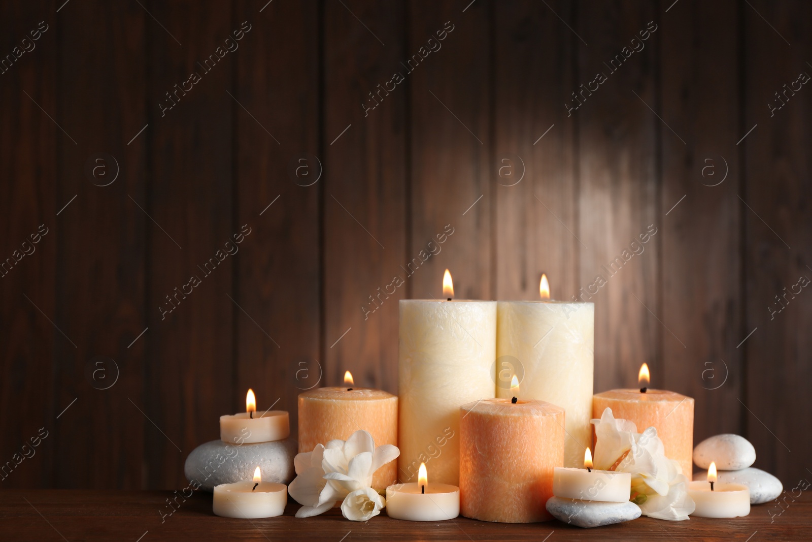 Photo of Beautiful composition with candles, flowers and stones on table against wooden background. Space for text