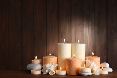 Beautiful composition with candles, flowers and stones on table against wooden background. Space for text