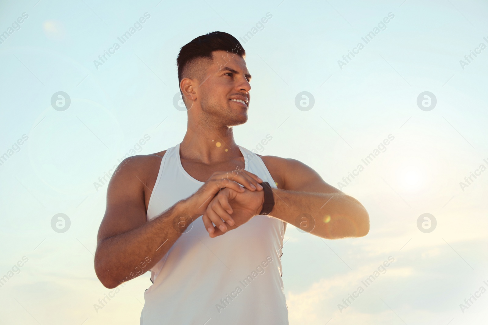 Photo of Man with athletic body checking fitness bracelet outdoors