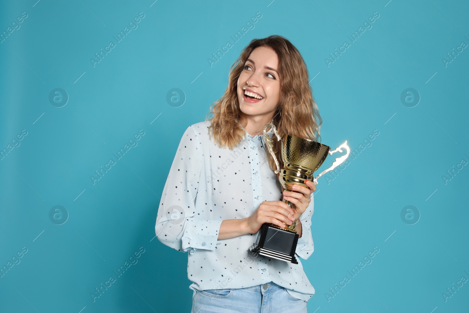 Photo of Portrait of happy young woman with gold trophy cup on blue background