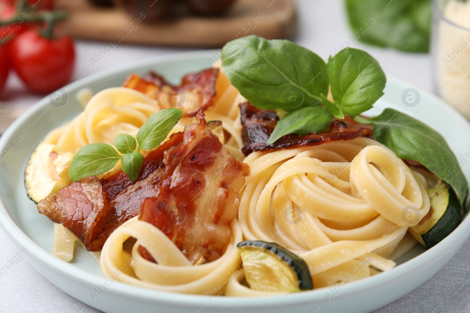 Photo of Tasty pasta with bacon and basil on light grey table, closeup