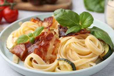 Photo of Tasty pasta with bacon and basil on light grey table, closeup