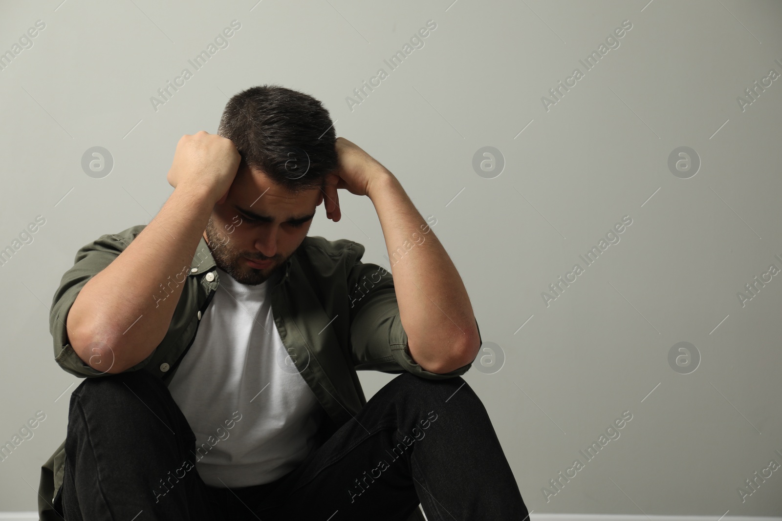 Photo of Sad man sitting near light grey wall. Space for text