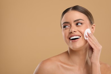 Beautiful woman removing makeup with cotton pad on beige background, space for text