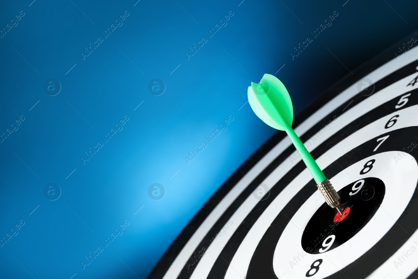 Photo of Green arrow hitting target on dart board against blue background. Space for text