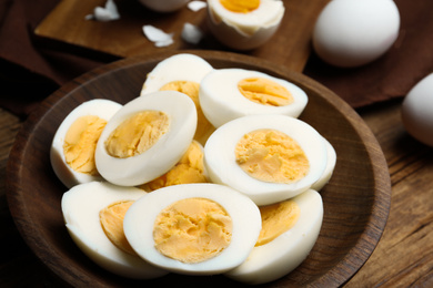 Photo of Cut hard boiled chicken eggs in wooden bowl on table