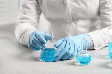 Photo of Scientist with flask of light blue liquid in laboratory, closeup