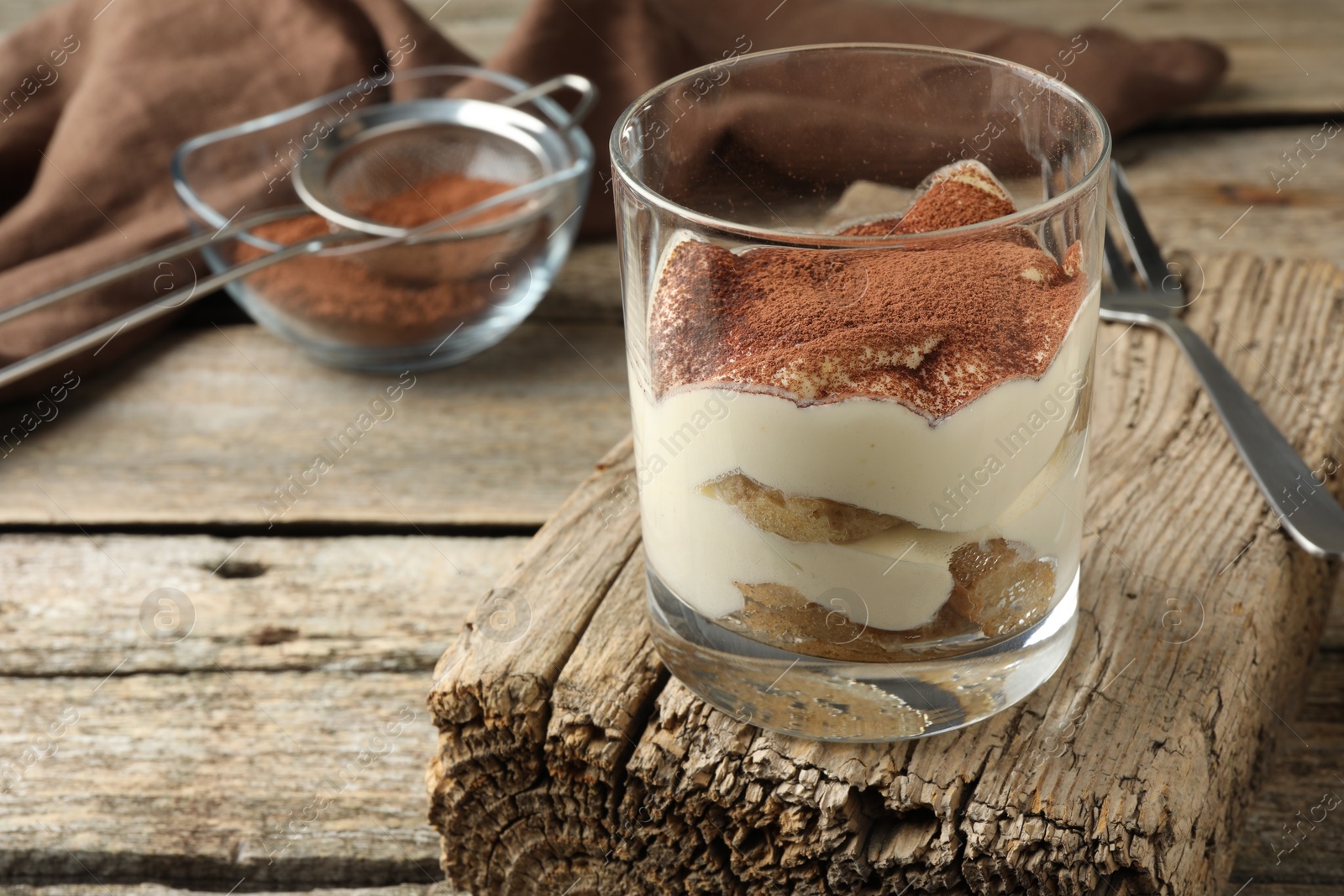 Photo of Delicious tiramisu in glass and fork on wooden table, closeup. Space for text