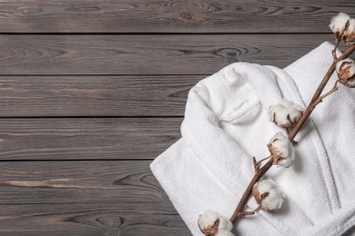 Photo of Flat lay composition with folded bathrobe and cotton flowers on wooden background, space for text