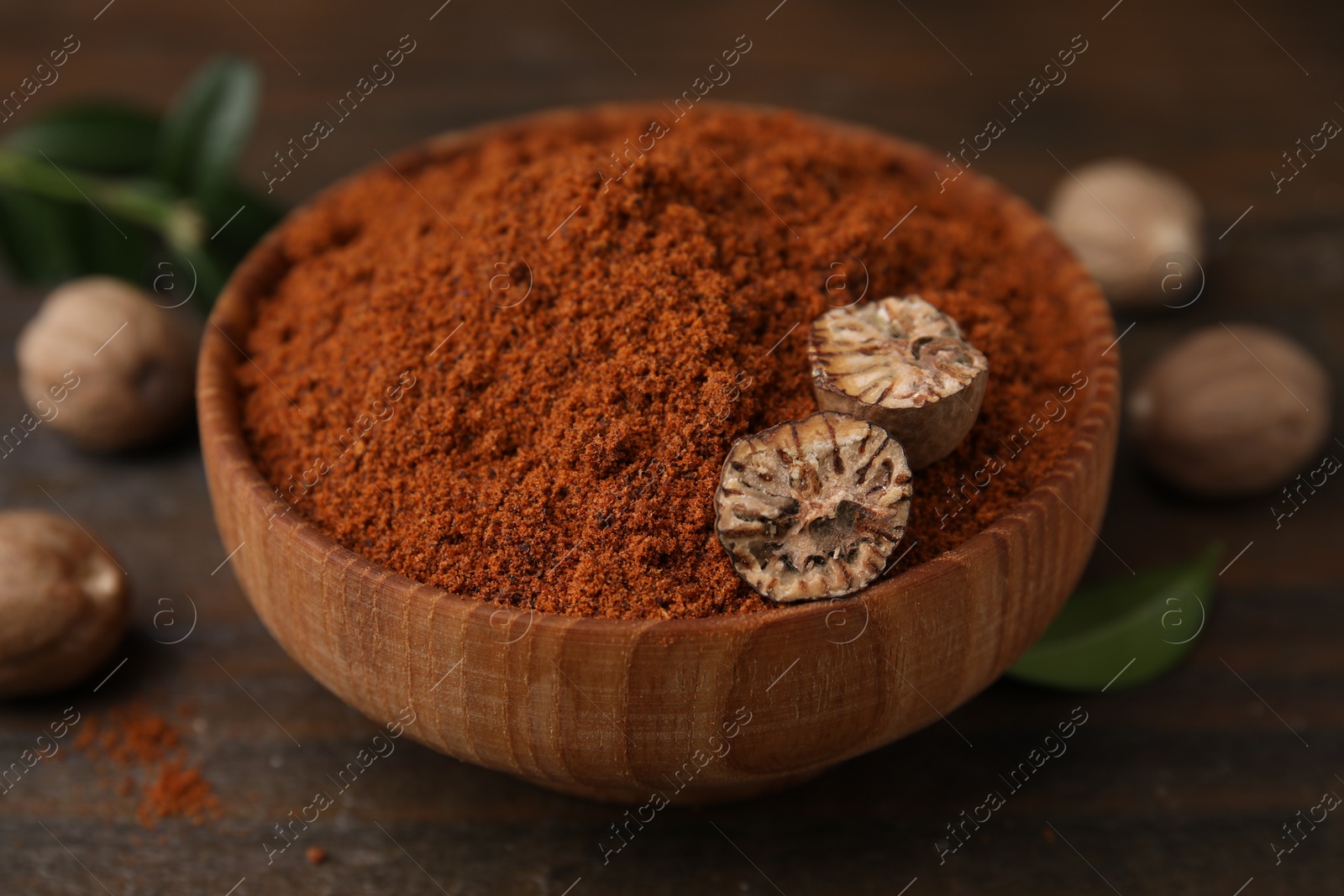 Photo of Nutmeg powder and halves of seed in bowl on wooden table, closeup