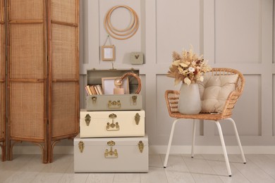 Photo of Wicker chair with dry flowers and storage trunks indoors. Interior design