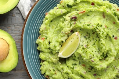 Delicious guacamole with lime and fresh avocado on grey wooden table, flat lay