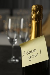 Photo of Note with phrase I Love You attached to bottle of champagne in room, closeup