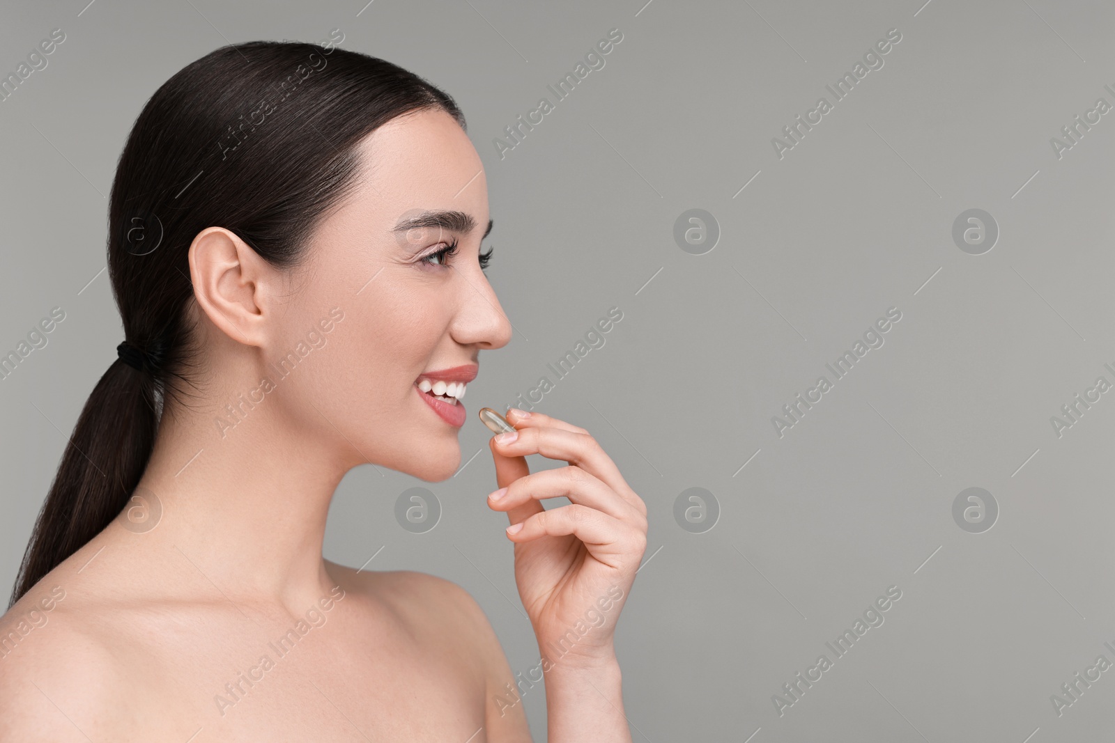 Photo of Beautiful young woman with vitamin pill on grey background. Space for text