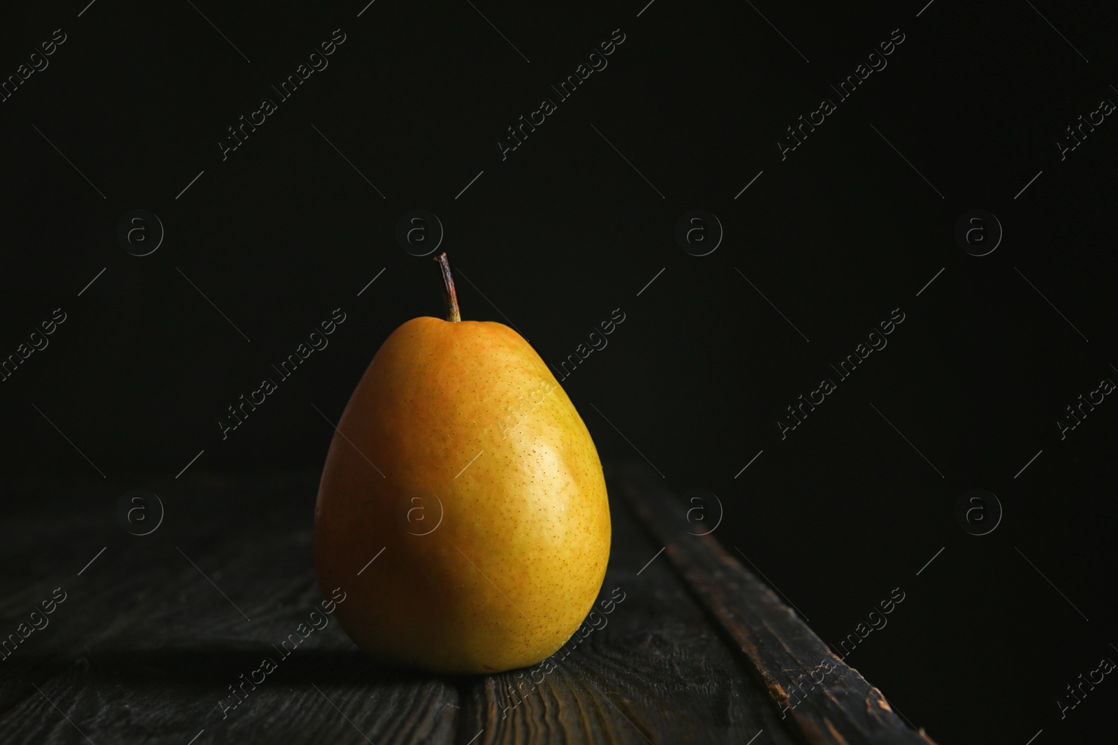 Photo of Ripe pear on wooden table against dark background. Space for text