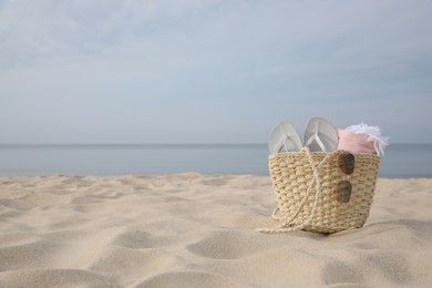 Photo of Beach bag with flip flops, towel and sunglasses on sandy seashore, space for text