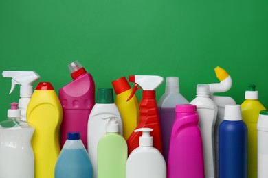 Many bottles of different detergents on green background. Cleaning supplies