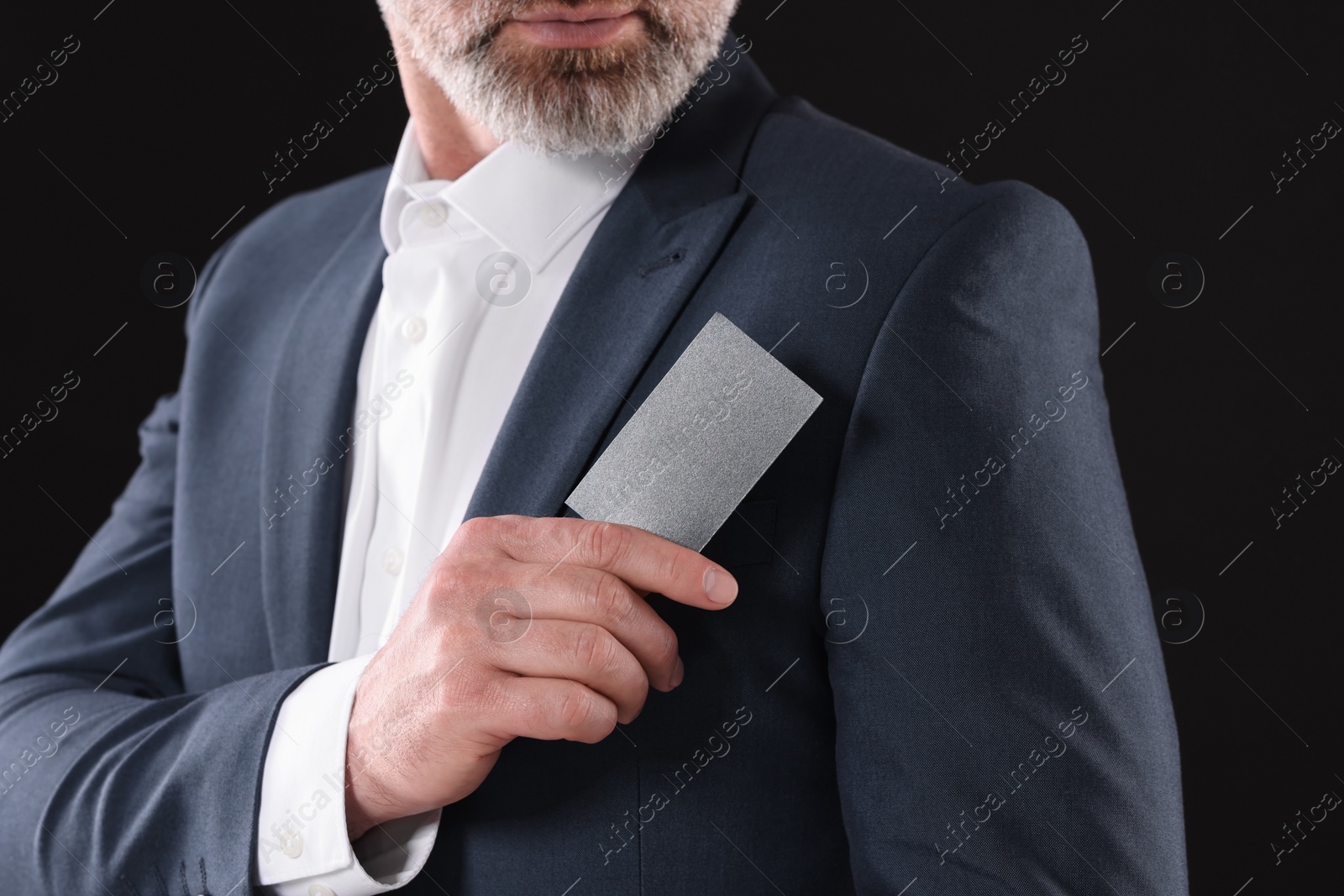 Photo of Businessman holding blank business card on black background, closeup