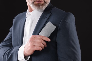 Photo of Businessman holding blank business card on black background, closeup