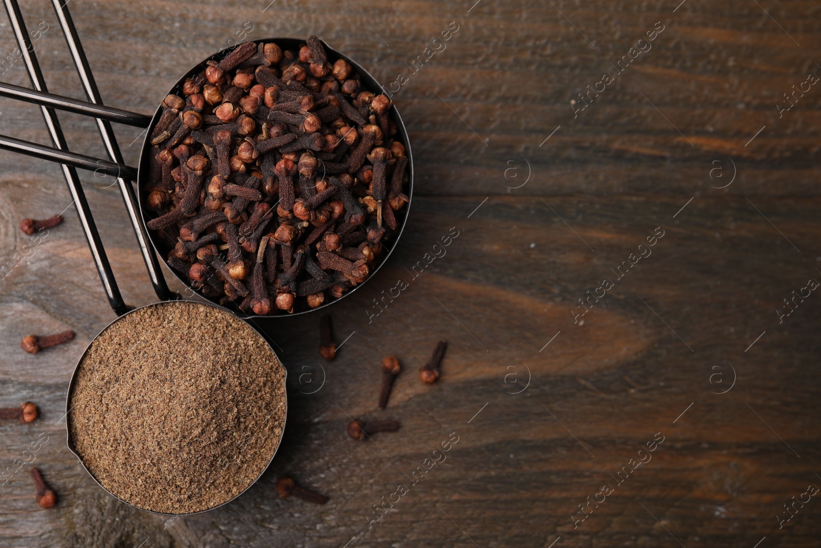 Photo of Aromatic clove powder and dried buds in scoops on wooden table, top view. Space for text