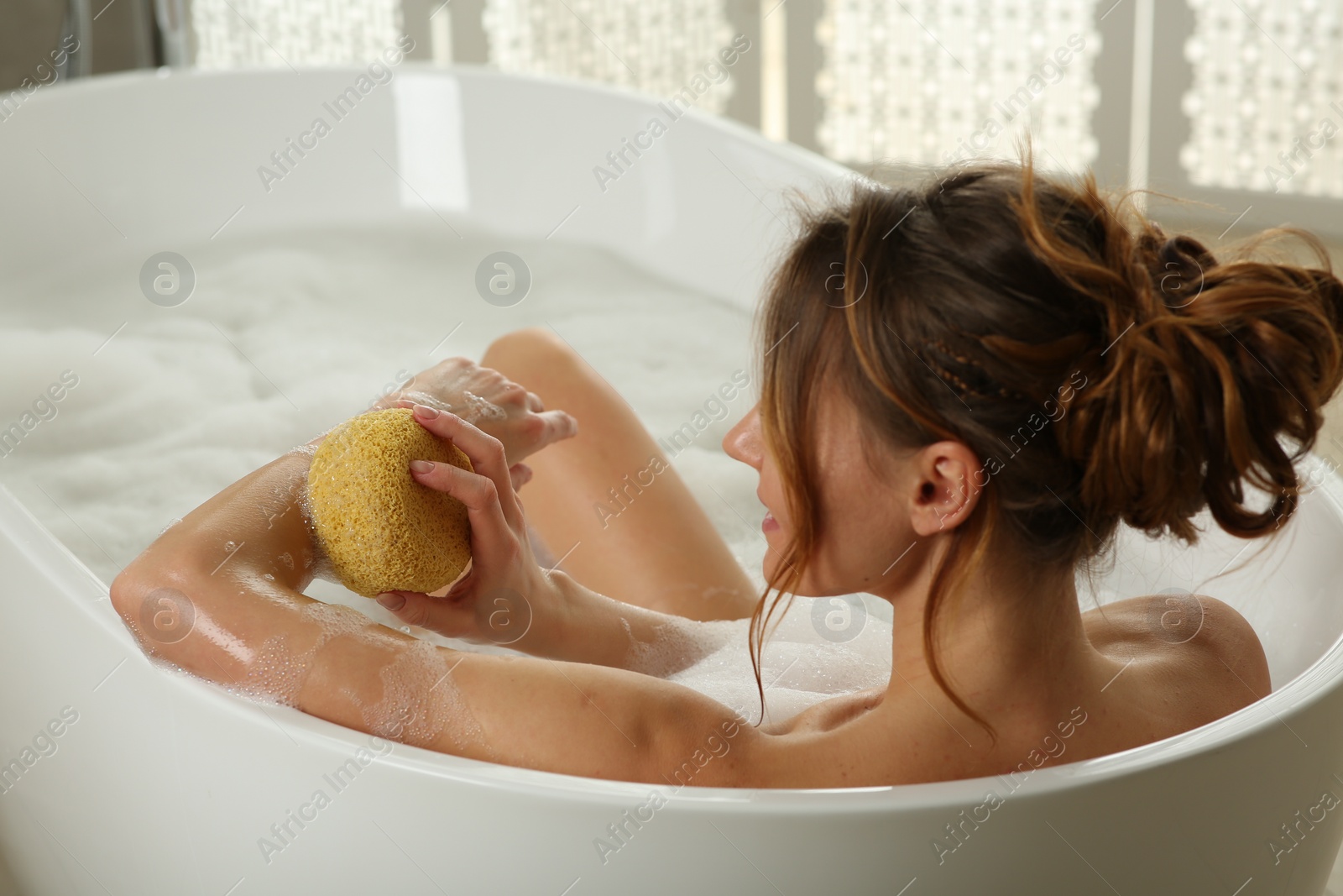 Photo of Woman rubbing her forearm with sponge while taking bath