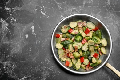 Delicious cooked Brussels sprouts with bacon in pan on marble table, top view. Space for text