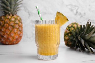 Tasty pineapple smoothie, whole and cut fruits on white table