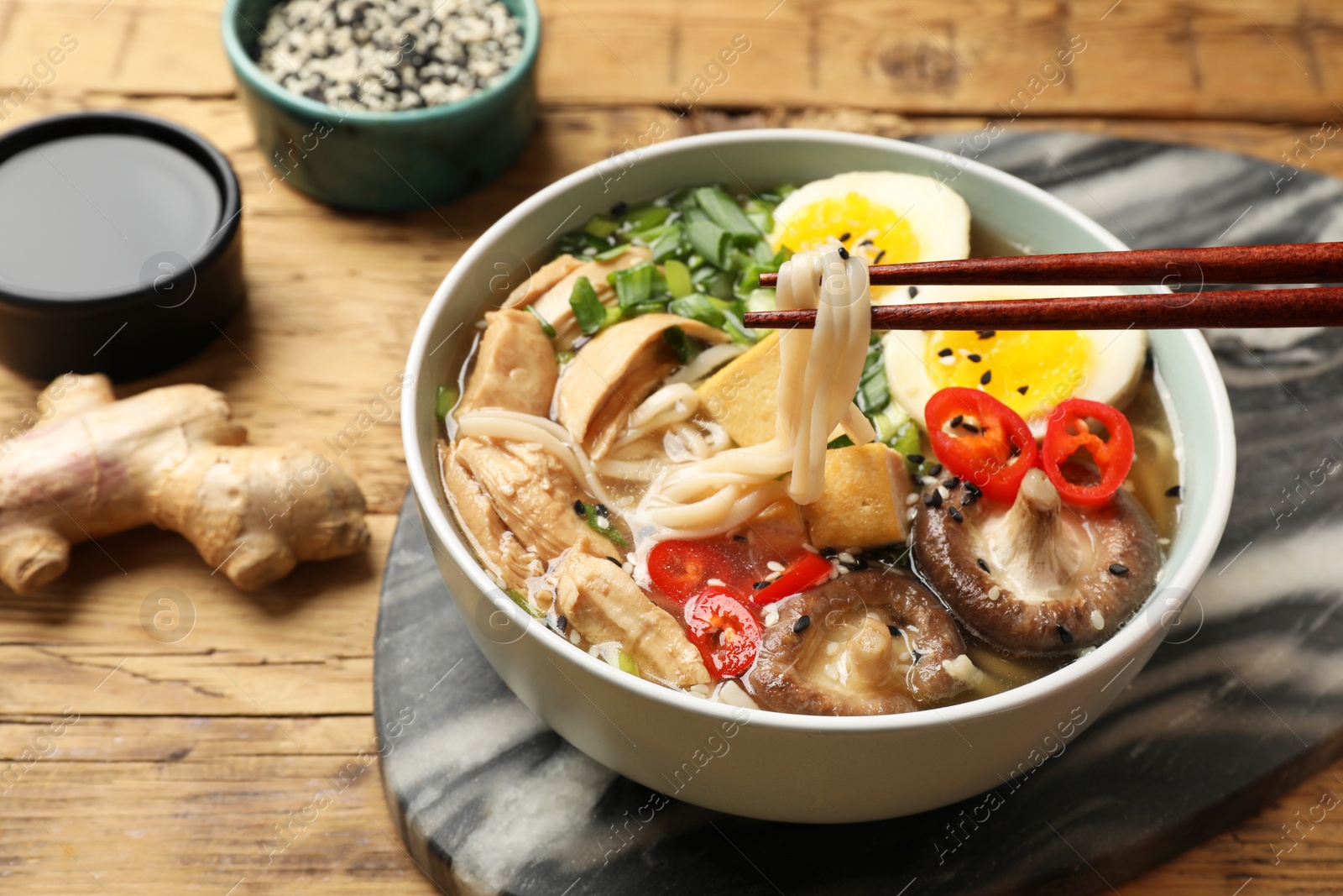 Photo of Eating delicious ramen with chopsticks on wooden table, closeup. Noodle soup