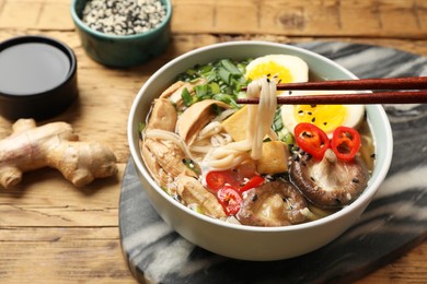 Photo of Eating delicious ramen with chopsticks on wooden table, closeup. Noodle soup