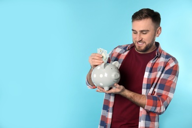 Photo of Happy young man putting money into piggy bank on color background. Space for text
