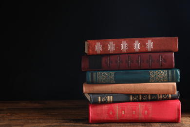 Photo of Collection of different books on wooden table against dark background. Space for text