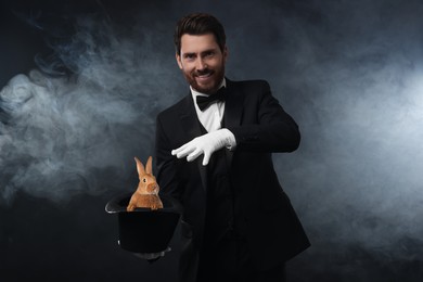 Image of Magician showing trick with top hat and rabbit in smoke on dark background