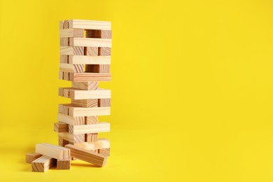 Photo of Jenga tower made of wooden blocks on yellow background, space for text
