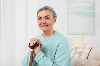 Senior woman with walking cane sitting on sofa at home