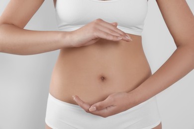 Woman in underwear holding something near her belly on light background, closeup. Healthy stomach