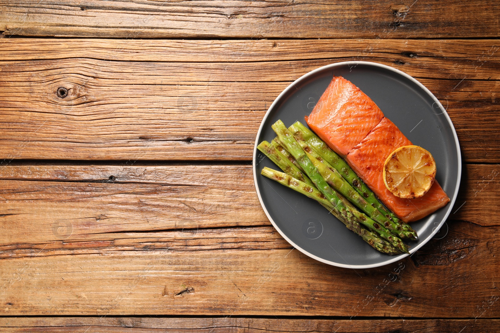 Photo of Tasty grilled salmon with asparagus and lemon on wooden table, top view. Space for text