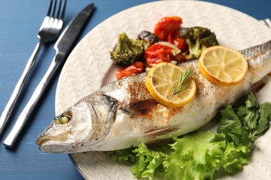 Photo of Delicious baked fish and vegetables served on blue wooden table, closeup