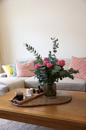 Beautiful bouquet of roses and eucalyptus branches in vase near candles on table at home. Space for text