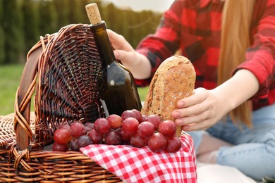 Photo of Girl taking bread from wicker picnic basket outdoors, closeup