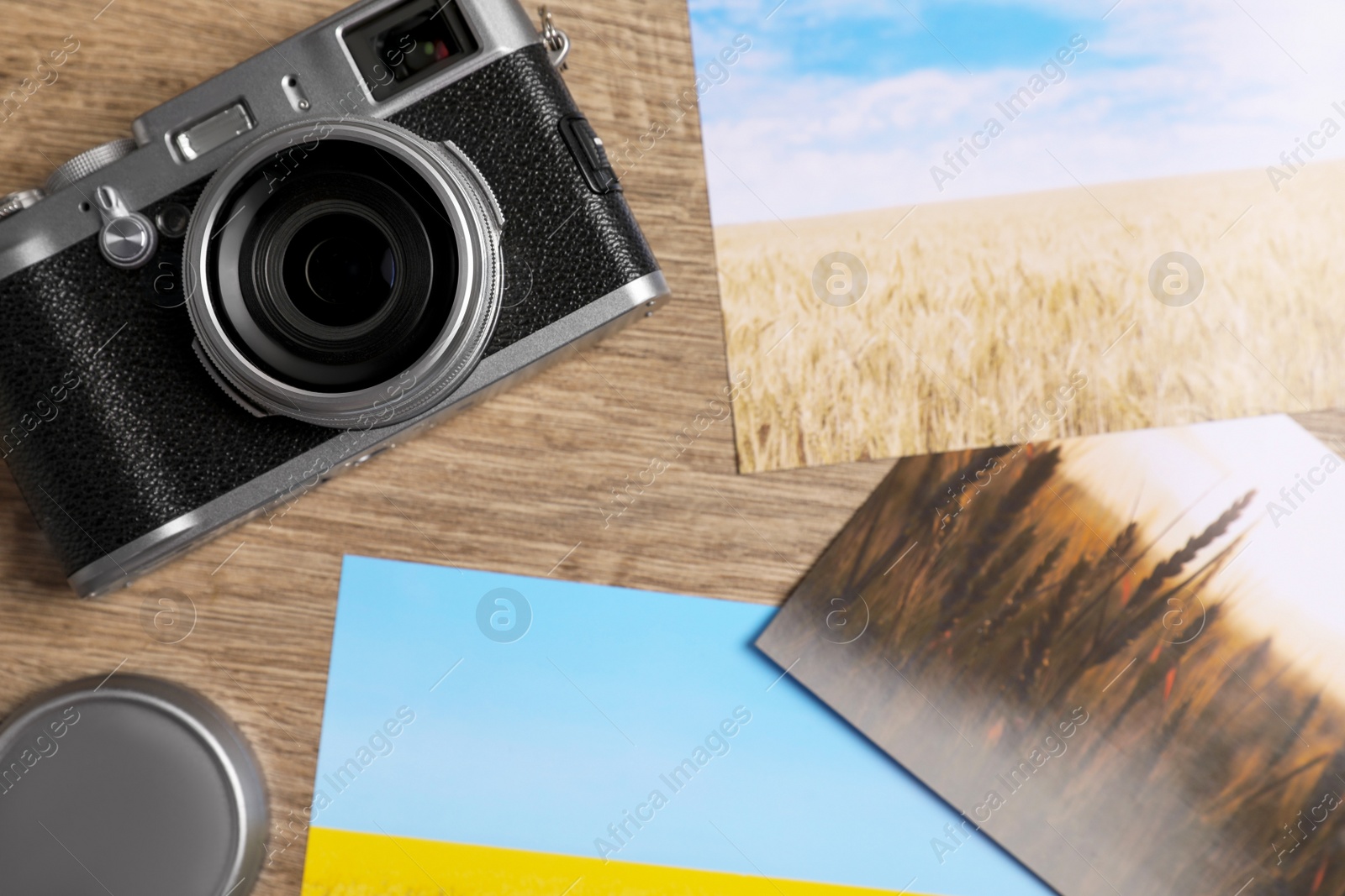 Photo of Vintage photo camera and beautiful printed pictures on wooden table, flat lay. Creative hobby