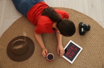 Photo of Woman using tablet with Black Friday announcement while lying on floor at home, above view