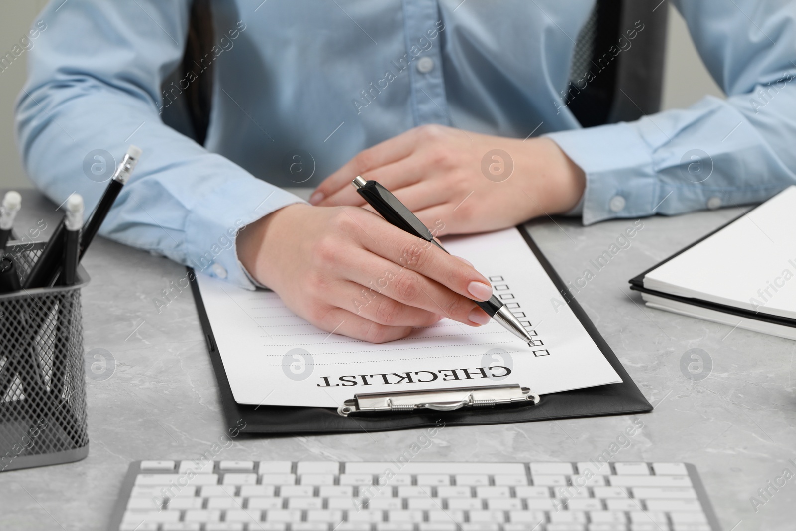 Photo of Woman filling Checklist at grey marble table, closeup