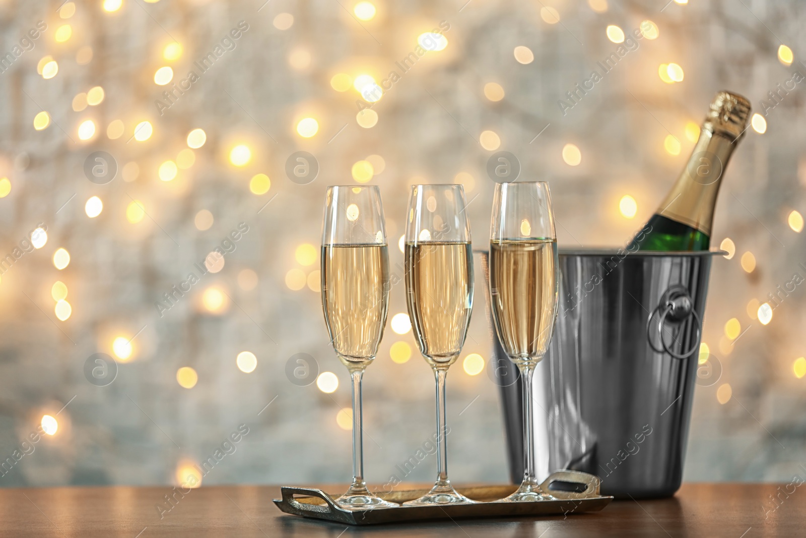 Photo of Glasses with champagne and bottle in bucket on table against blurred lights