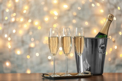 Photo of Glasses with champagne and bottle in bucket on table against blurred lights